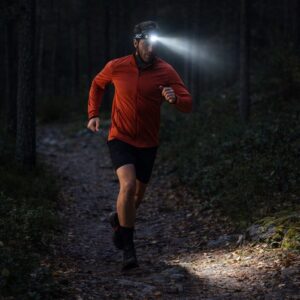 Juoksija käyttämässä otsalamppua pimeällä metsäpolulla – paras otsalamppu juoksuun 2026.